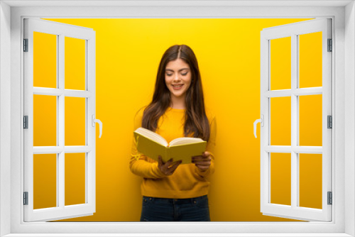 Teenager girl on vibrant yellow background holding a book and enjoying reading