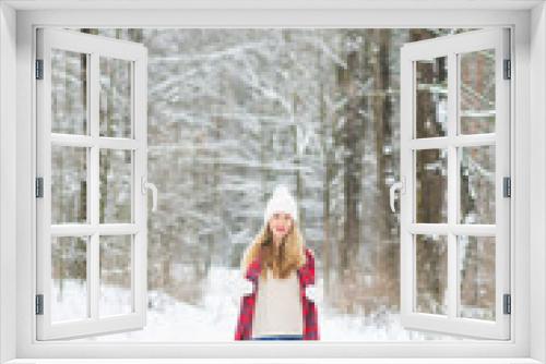 Young happy woman in winter clothes walks in the snowy forest