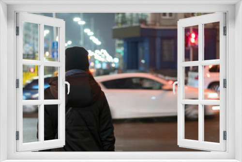 Girl waiting to cross the road while pedestrian traffic lights is red in the night city. close up.