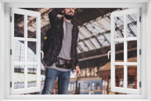 stylish bearded hipster tourist with backpack behind his shoulder on the platform of the railway station with a metal vault
