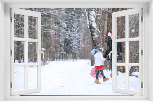 A winter fairy tale, a young mother and her daughter ride a sled in the forest. A girl on a sled with gifts on the eve of the new year in the park.