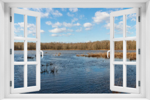 Fototapeta Naklejka Na Ścianę Okno 3D - White puffy clouds float in a sunny blue sky over the rippling waters of a Virginia marsh.