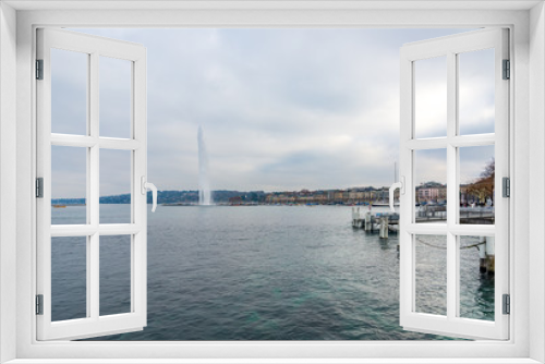 Fototapeta Naklejka Na Ścianę Okno 3D - Outdoor scenery of THE JET D'EAU, famous water jet fountain on Geneva lake, and tranquil landscape of Lake Geneva, embankment and harbor along waterside with background of overcast sky in Switzerland.