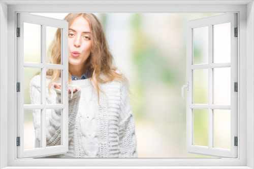 Beautiful young blonde woman wearing winter sweater over isolated background looking at the camera blowing a kiss with hand on air being lovely and sexy. Love expression.