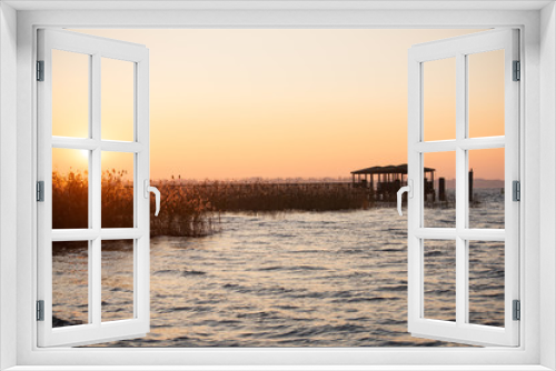 Fototapeta Naklejka Na Ścianę Okno 3D - Beautiful sunset on the abandoned lake pier. Wooden structure for panoramic access to the lake. Sun on the horizon, silhouette of bridge with sunset. Colorful sky with clouds in the evening.