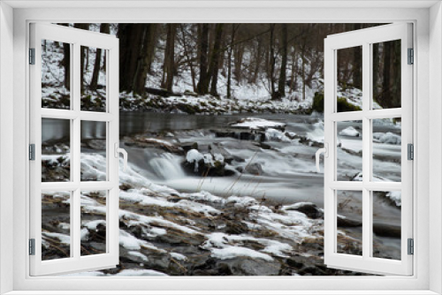 Fototapeta Naklejka Na Ścianę Okno 3D - smooth motion of wild water in a river in winter with snow and ice on rocks and stones in the beautiful nature of a forest