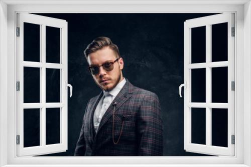 An elegantly dressed young man in sunglasses against a dark textured wall