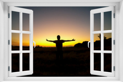Fototapeta Naklejka Na Ścianę Okno 3D - Silhouette Asian young man open arm is standing on grass city country home of field with sunset light and beautiful sky twilight sky and cloud. Success,  happytime.