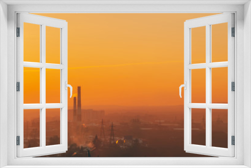 Fototapeta Naklejka Na Ścianę Okno 3D - Smog among silhouettes of buildings on sunrise. Smokestack in dawn sky. Environmental pollution on sunset. Harmful fumes from stack above city. Mist urban background with warm orange yellow sky.