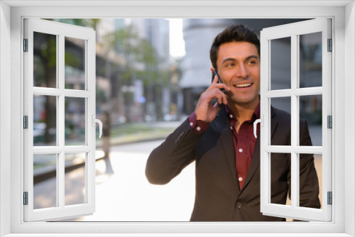 Happy Hispanic businessman thinking while talking on the phone outdoors