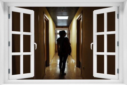 A young woman with a backpack is walking along the corridor of the hotel to her room. Silhouette of a girl with a backpack
