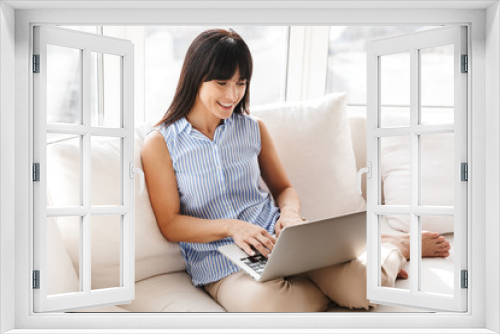 Portrait of smiling woman typing and using silver laptop while sitting on couch