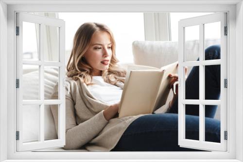 Blonde woman posing sitting indoors at home reading book.