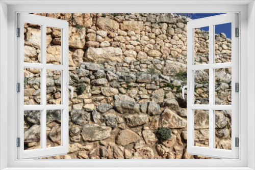 Fototapeta Naklejka Na Ścianę Okno 3D - Background of ancient Greek rock wall with vegetation and moss growing between some rocks and a corner of blue sky showing