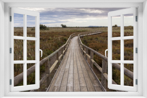 Fototapeta Naklejka Na Ścianę Okno 3D - view of a wooden walkway between the reeds and the vegetation of a wetland on cloudy day