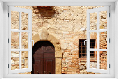 Fototapeta Naklejka Na Ścianę Okno 3D - Dark wooden double doors in an ancient stone wall, with a window with bars on it