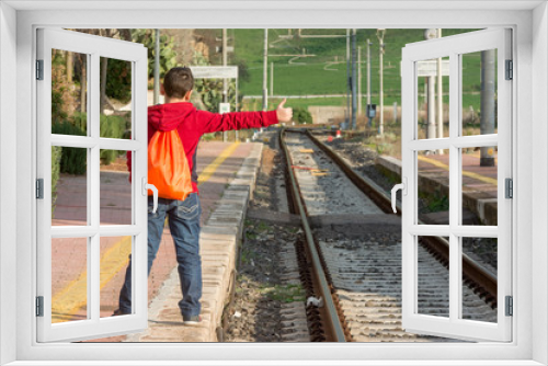 Young hitchhiker waiting of the train, standing on railway