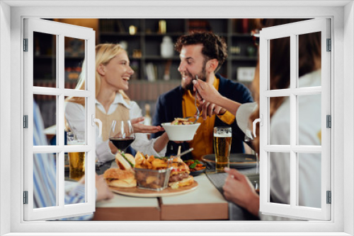 Multiethnic friends sitting at restaurant, drinking alcohol, chatting and having burgers for dinner.