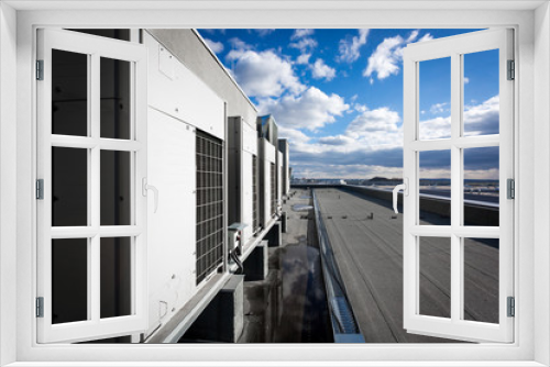 Fototapeta Naklejka Na Ścianę Okno 3D - A series of gradually receding air conditioning units on the roof with blue sky and clouds in the background. 