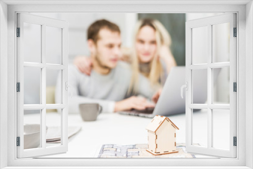 Lovely young couple, using a laptop and choosing a new apartment. Layout of the house in the foreground.