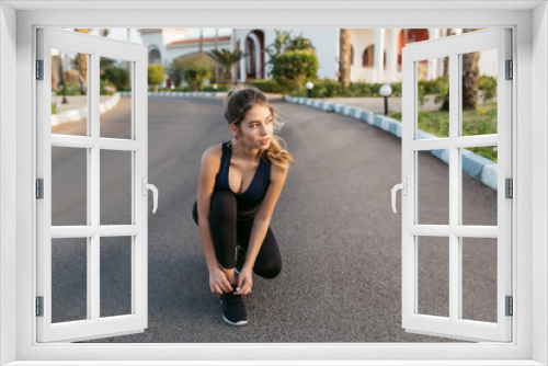 Motivated young pretty woman lacing shoelaces on sneakers on street with palm trees. Sunny morning in tropical city, preparing to run, workout, fitness, training