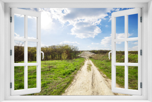 Fototapeta Naklejka Na Ścianę Okno 3D - Beautiful view of road in the field and green forest and blue cloudy sky and top of the hill. Spring rural landscape.