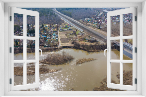 Fototapeta Naklejka Na Ścianę Okno 3D - Aerial view of the river with a railway bridge, a small village with small crowbars. Streets, shops and crossroads on a sunny autumn day. Helicopter drone shot.