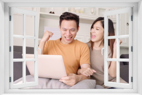 Asian couple using laptop for search web in living room at home, sweet couple enjoy love moment while lying on the sofa when relax at home. Lifestyle couple relax at home concept.