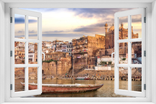 Fototapeta Naklejka Na Ścianę Okno 3D - Ancient Varanasi city architecture at sunset with view of Ganges river ghat and wooden boat on river Ganga