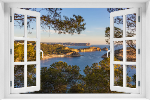 Fototapeta Naklejka Na Ścianę Okno 3D - A wonderful view over the cliffs and bays of the northern Costa Blanca near the city of Javea in the sunshine and blue sky with trees and branches in the foreground.