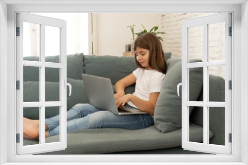 Beautiful cute charming young girl playing and surfing the internet on laptop at home