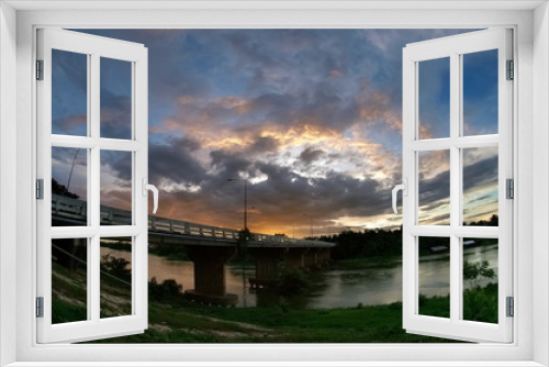 Fototapeta Naklejka Na Ścianę Okno 3D - sunset at Mae Klong river, view of the bridge cross the river with dark clouds and yellow sun light in the sky background, Ban Pong District, Ratchaburi, Thailand.
