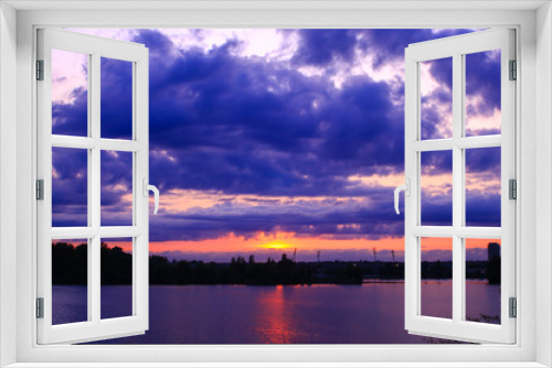 Fototapeta Naklejka Na Ścianę Okno 3D - Awesome sunset over the city. Very colorful horizon with large cumulonimbus.  Dark sky with the rays of the sun piercing and reflected in the water of a lake