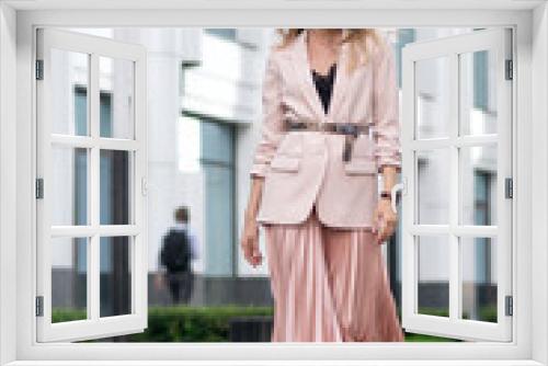 White girl walks down the street in a pink jacket, pleated skirt and sneakers. The territory of the business center. Great mood. Growth portrait.