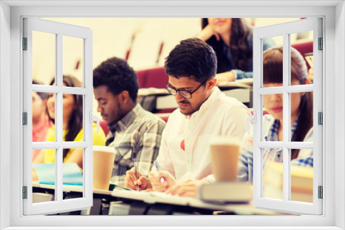 education, high school, university, learning and people concept - group of international students with notebooks and coffee writing test in lecture hall