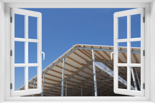 Fototapeta Naklejka Na Ścianę Okno 3D - Roof structure consisting of a metal frame, wooden beams and foam insulation against a blue sky. Agricultural constructions. The roof of the new barn.