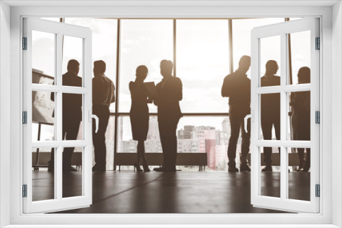 Silhouettes of people against the window. A team of young businessmen working and communicating together in an office. Corporate businessteam and manager in a meeting.