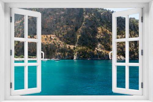 Fototapeta Naklejka Na Ścianę Okno 3D - Secluded beach surrounded by valley cliffs in a tranquil bay with turquoise water and sailing boats at sunrise, Oludeniz, Turkey panoramic