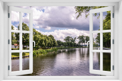 Fototapeta Naklejka Na Ścianę Okno 3D - Sluis, the Netherlands -  June 16, 2019: Reflecting water of canal to Damme in Belgium, with curtains of green trees on sides, under a storm approaching cloudscape.