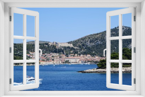 Fototapeta Naklejka Na Ścianę Okno 3D - A faraway view from the ferry of the town of Hvar, on Hvar Island, Croatia.  It is a beautiful sunny summer day and the adriatic sea is calm.  Another boat is passing by the ferry.