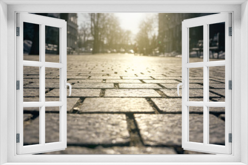 Fototapeta Naklejka Na Ścianę Okno 3D - Paving tiles illuminated by sunlight background. Paving slabs close-up on the background of streets, trees and sky in blur.