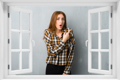 Young redhead girl over grunge wall surprised and pointing side