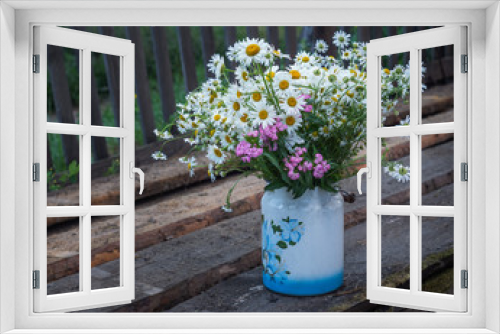 Fototapeta Naklejka Na Ścianę Okno 3D - A large bouquet of wild flowers of daisies and carnations in a can with a pattern, standing outdoors on old boards.