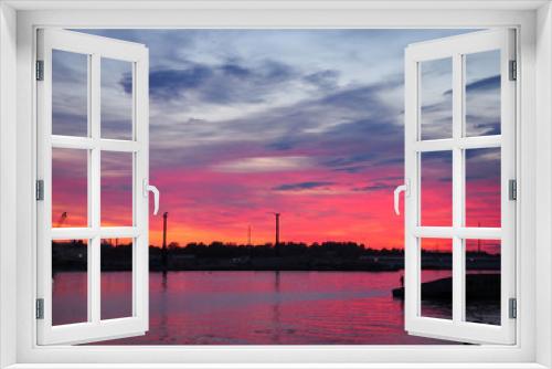 Fototapeta Naklejka Na Ścianę Okno 3D - A beautiful red and yellow sunset over the city is reflected in the water of the river with the .silhouette of a fisherman in the background. Panoramic landscape on the dusk.
