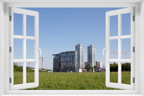Fototapeta Naklejka Na Ścianę Okno 3D - Several Yellow hoisting cranes against the blue sky. The cranes are lifting the load to the top of the house construction.