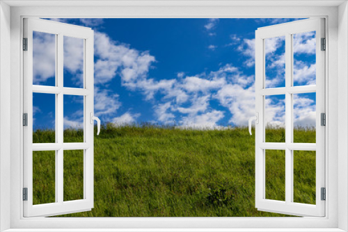 Fototapeta Naklejka Na Ścianę Okno 3D - A beautiful summer hill landscape scene. The hill is covered in lush green grass topped with a bright blue sky and a scattering of fluffy brilliant white cumulus clouds.