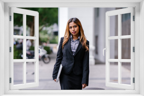 Portrait of a beautiful, young and attractive Singaporean Malay Asian woman in a business suit walking in a city in Asia during the day with her laptop computer. She is smiling confidently.
