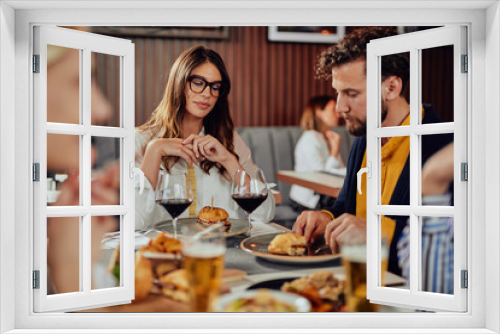 Multiethnic friends sitting at restaurant, drinking alcohol, chatting and having burgers for dinner.