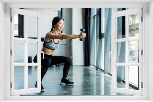 happy young sportswoman holding dumbbells and doing squat exercise