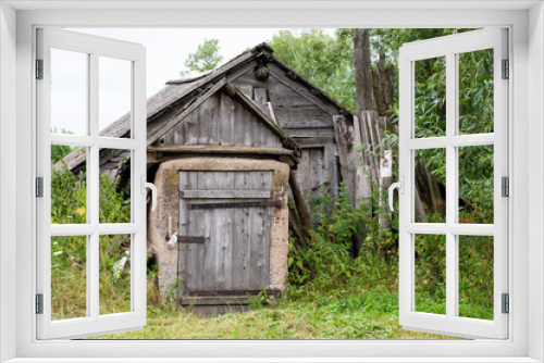 Fototapeta Naklejka Na Ścianę Okno 3D - Wooden abandoned farmhouse with peeling paint and broken windows in rural countryside in summer